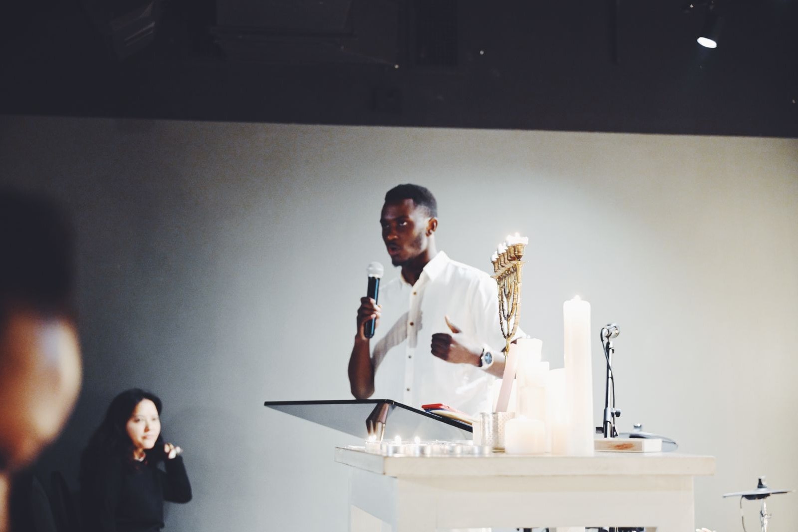 Alexander Hwande speaking into a microphone at a lectern, with candles in front of him