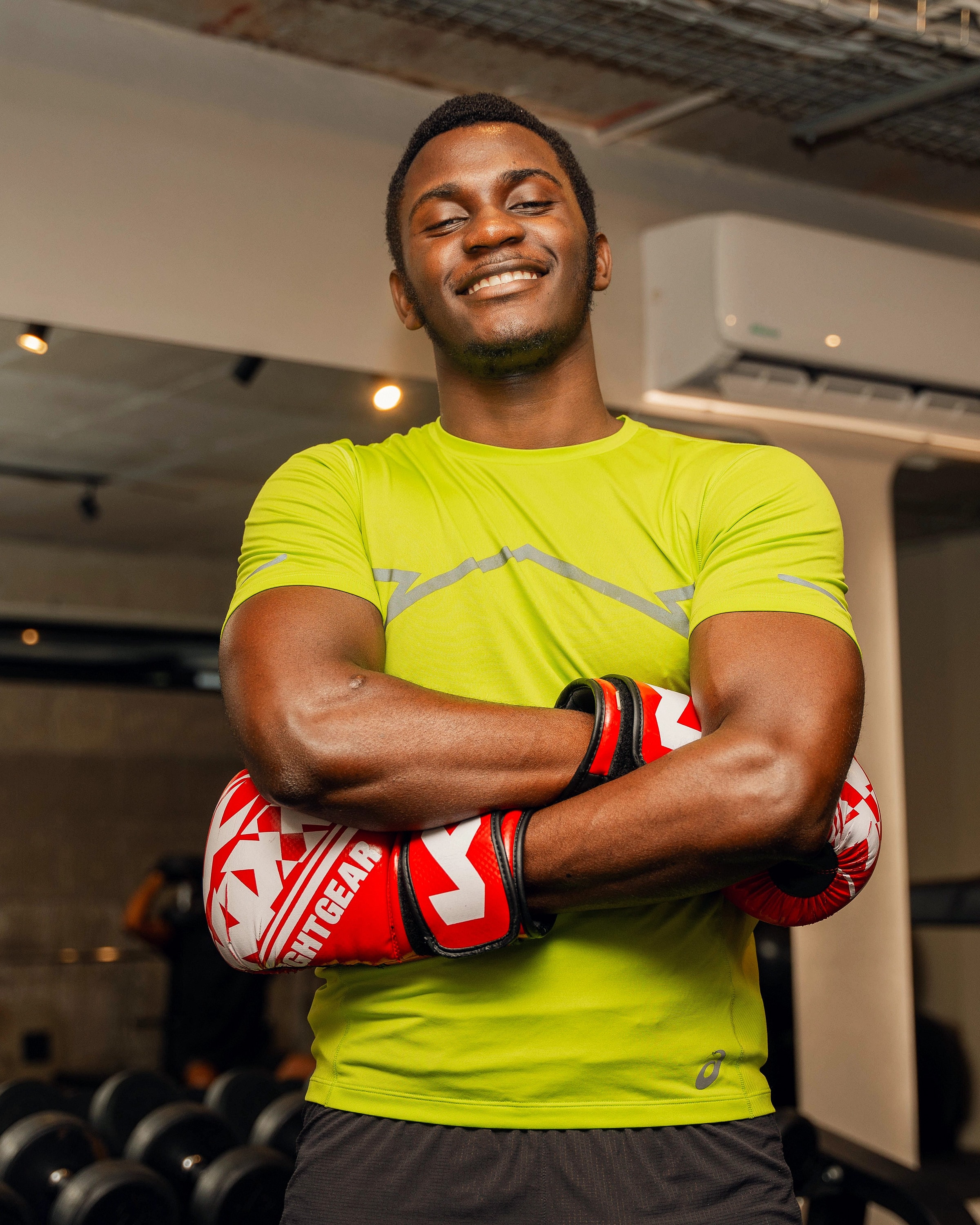 Alexander Hwande in a gym, smiling, arms folded in boxing gloves