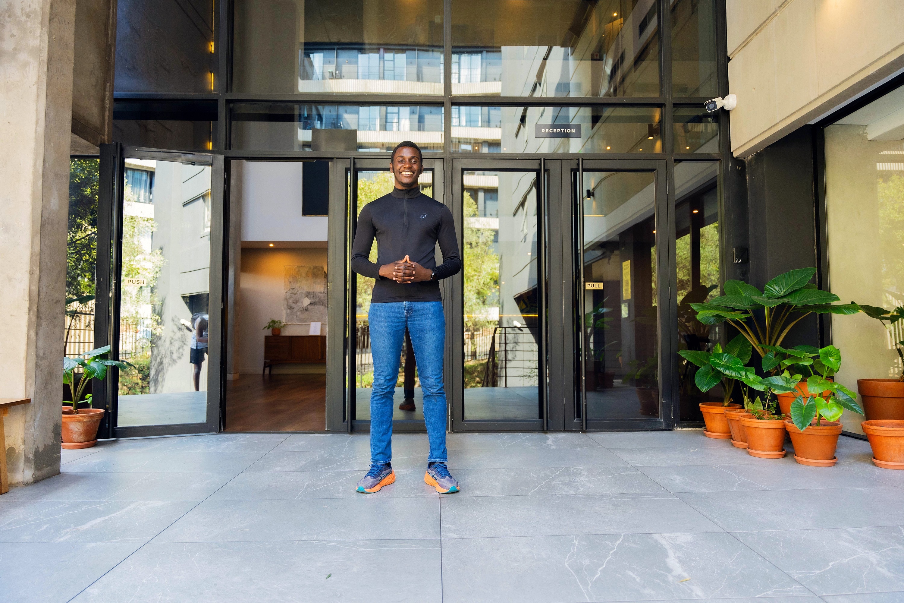 Alexander Hwande standing at the entrance of a building, smiling, with his hands together