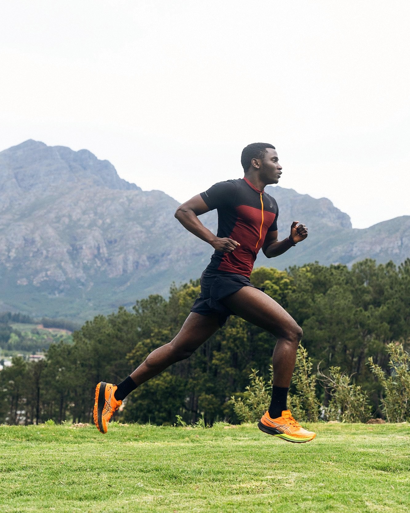 Alexander Hwande in full stride across a grass slope, with mountains behind him